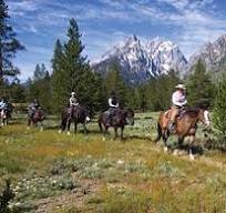 Guided horseback riders on a trail through wildflowers below the Grand Tetons