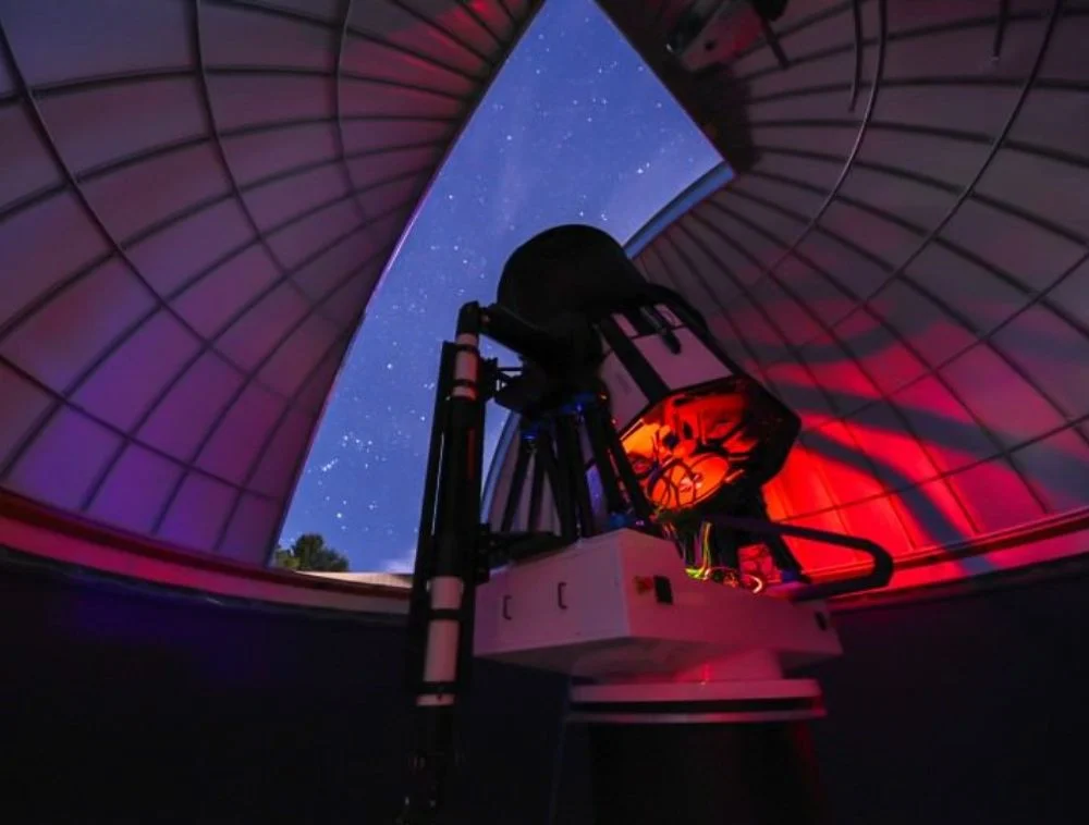 Professional telescope inside an observatory dome with a starry night sky visible above Jackson Hole