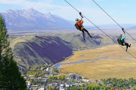 Two riders ziplining side by side above Jackson Hole with the Teton Range in the background